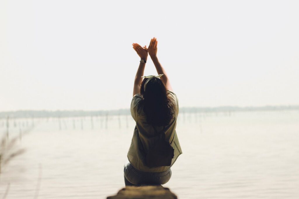 A serene moment of a woman raising her arms by a calm lake, embracing nature's tranquility.