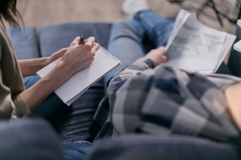 A person writing notes in a notepad while sitting on a couch, studying or reading.