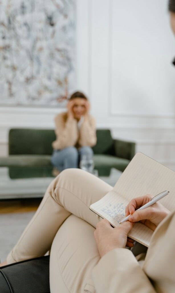 A therapist takes notes in a modern office setting during a therapy session with a patient.