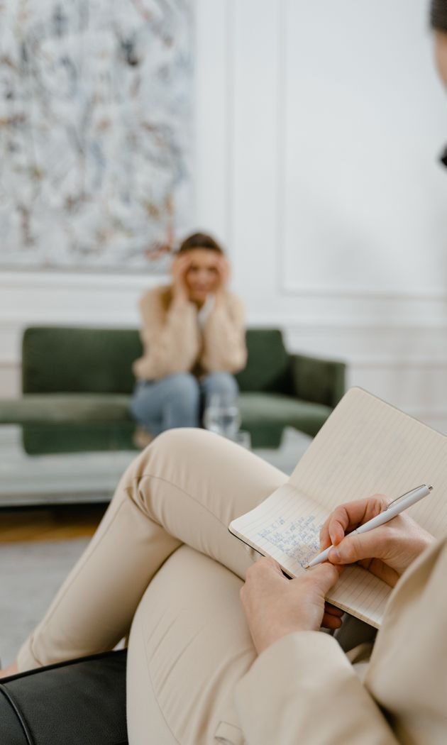 A therapist takes notes in a modern office setting during a therapy session with a patient.